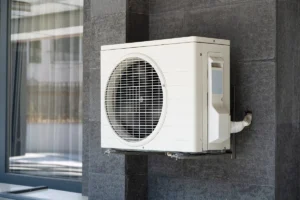 Outdoor wall-mounted mini split condenser installed on a dark exterior wall.