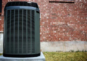 Outdoor residential heat pump unit installed on a concrete pad beside a brick home exterior. Best for blogs about heat pump systems, residential HVAC replacement, outdoor HVAC units, high-efficiency heating and cooling, heat pump installation, and AC vs heat pump topics.