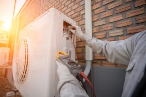 Technician testing electrical components on an outdoor mini split unit with a multimeter.